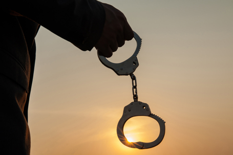 hand holding  handcuffs silhouetted against a sunset